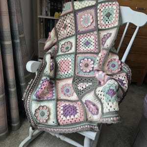 May include: A handmade crochet blanket featuring a patchwork of square motifs in pastel pink, mint green, cream, and lavender, joined by a dark gray border. The blanket includes floral-inspired circular patterns and the text Little Green Bear.