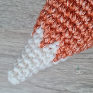 May include: Close-up of a crocheted fox tail with a white tip and orange body.