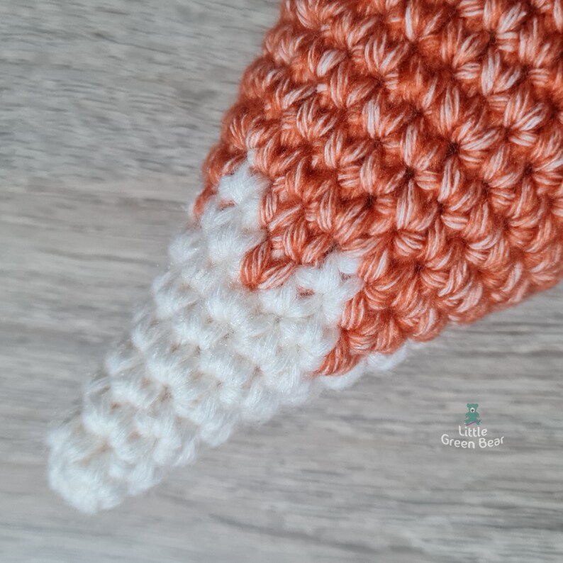 May include: Close-up of a crocheted fox tail with a white tip and orange body.