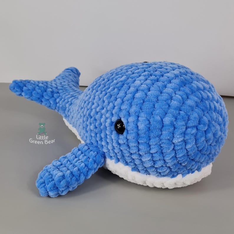 May include: A blue crocheted whale plush toy with white trim around the mouth and black eyes.