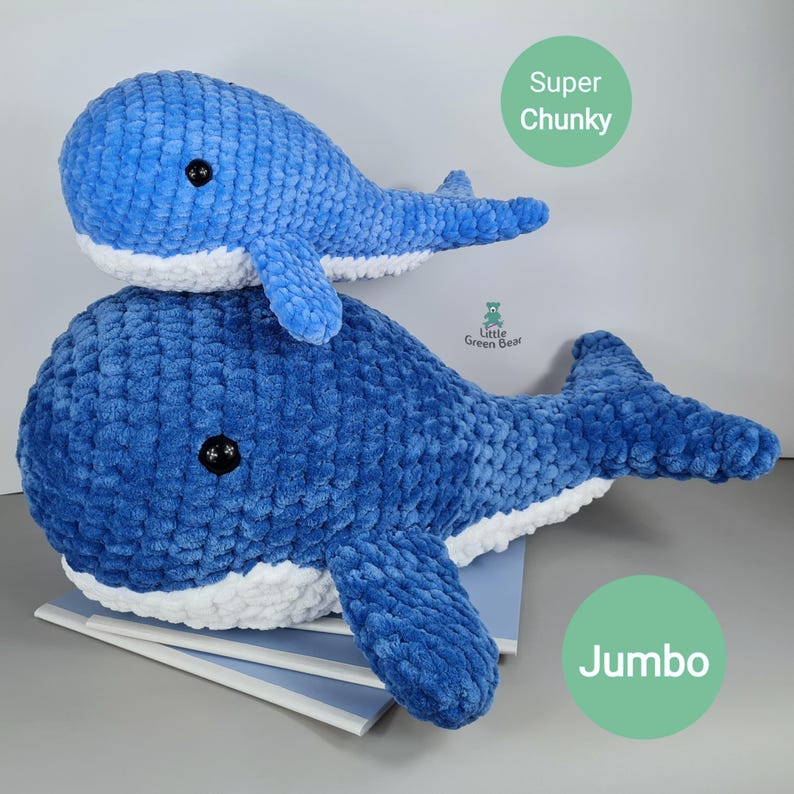 May include: Two crocheted whale plushies, one blue and white jumbo whale and a smaller blue and white super chunky whale. The whales are sitting on a stack of books. The text "Jumbo" and "Super Chunky" are written on the image.