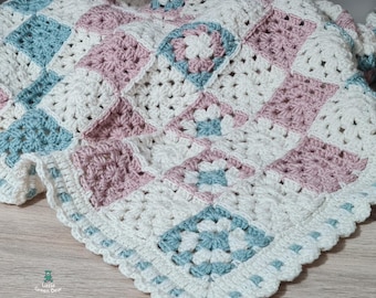 May include: A handmade crochet blanket in a granny square pattern. The blanket features squares of white, light blue, and pink. The edges are scalloped. The blanket is made of soft yarn and is suitable for a baby or child.