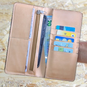 May include: A brown leather wallet with multiple card slots, a zippered compartment, and a slot for a phone. The wallet is open and shows a phone, cash, and credit cards.