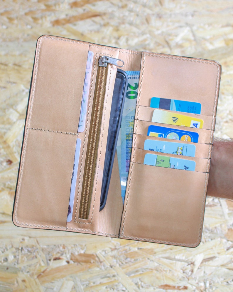 May include: A brown leather wallet with multiple card slots, a zippered compartment, and a slot for a phone. The wallet is open and shows a phone, cash, and credit cards.
