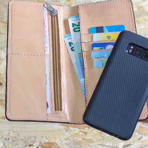 May include: A brown leather wallet with a zipper closure, containing cash and credit cards. A black phone case is next to the wallet.