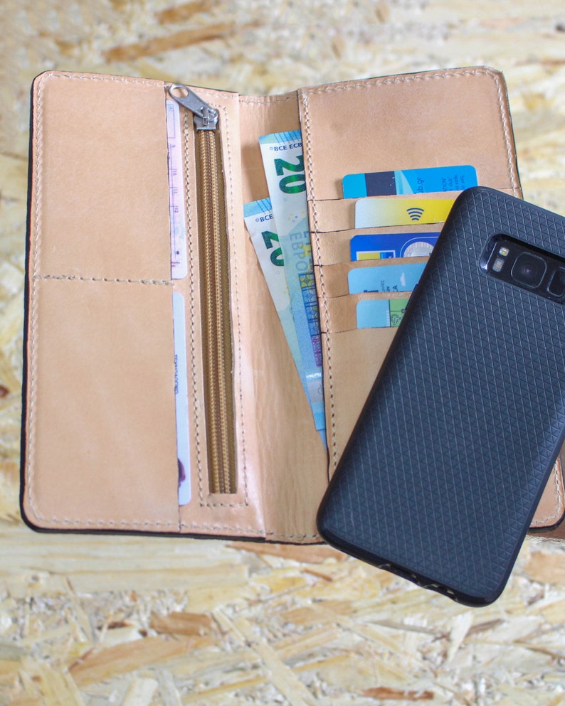 May include: A brown leather wallet with a zipper closure, containing cash and credit cards. A black phone case is next to the wallet.