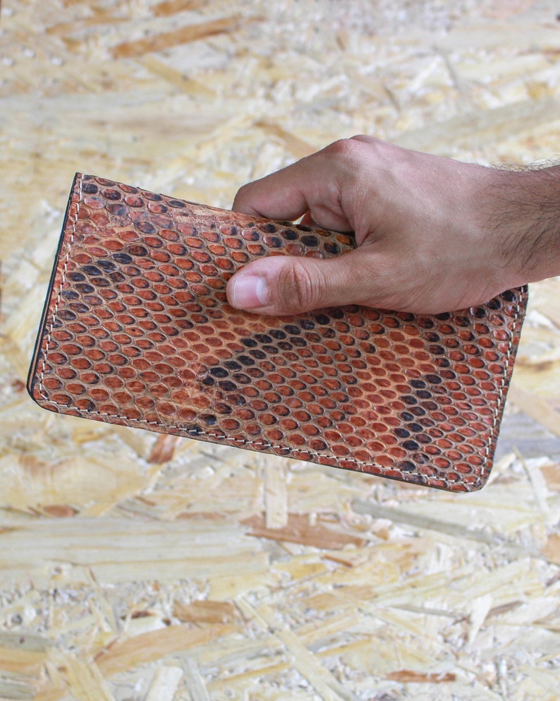 May include: A brown leather wallet with a snakeskin pattern. The wallet is held in a hand.