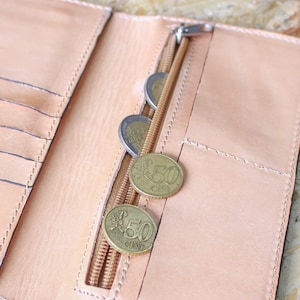 May include: A light brown leather wallet with a zippered pocket and several euro coins inside. The coins are 50 cent pieces.