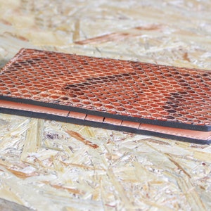 May include: A brown leather wallet with a snakeskin pattern. The wallet is closed and lying on a wood surface.