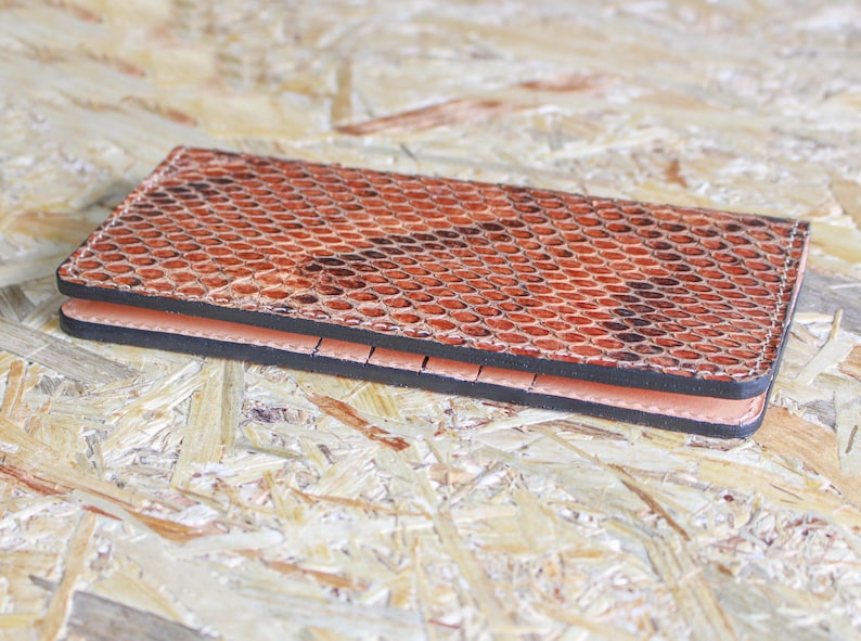 May include: A brown leather wallet with a snakeskin pattern. The wallet is closed and lying on a wood surface.