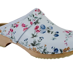 Pode incluir: Sapatos de couro branco com estampa floral e salto de madeira. Os sapatos têm uma tira na parte superior.