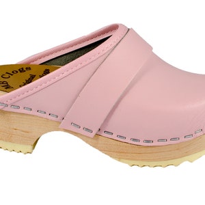 May include: Pink leather clogs with a wooden sole and a strap across the top. The clogs have a stitched edge and the text "MB Clogs Original" is visible on the side.