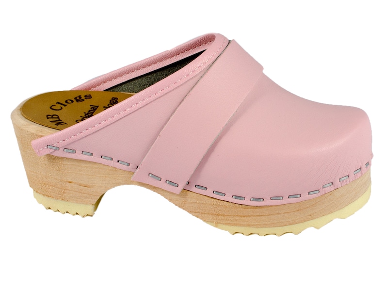 May include: Pink leather clogs with a wooden sole and a strap across the top. The clogs have a stitched edge and the text "MB Clogs Original" is visible on the side.