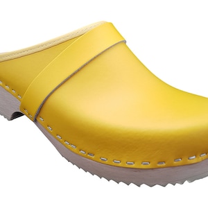 Pode incluir: Um par de tamancos de couro amarelo com sola de madeira e uma costura ao redor da borda.