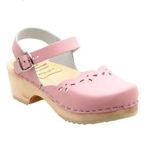 May include: Pink leather clog with a wooden heel and a buckle ankle strap. The clog has a scalloped edge and cutouts.