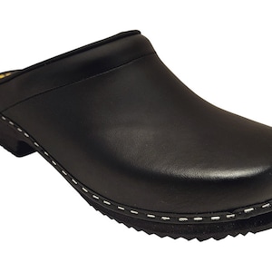 Pode incluir: Sapatilha de couro preta com um detalhe de costura branca ao redor da sola. A sapatilha tem a ponta fechada e um salto baixo.