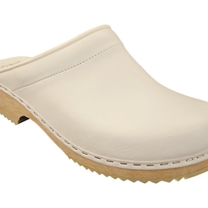 Pode incluir: Sapatos de couro branco com sola de madeira. Os sapatos têm um design simples e são um estilo clássico.