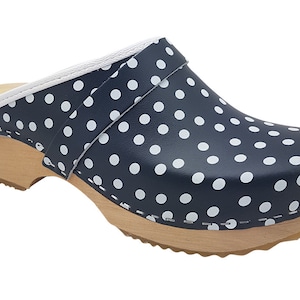 Pode incluir: Tamanco azul marinho com bolinhas brancas. O sapato tem sola de madeira e uma borda branca na parte superior. O padrão de bolinhas cobre toda a parte superior do sapato.