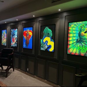 Peut inclure: Cinq affiches de film rectangulaires sont présentées dans des cadres lumineux sur un mur lambrissé sombre. Les affiches présentent divers personnages animés et de super-héros, dont une chenille verte avec le texte A Bug's Life et un dinosaure vert.