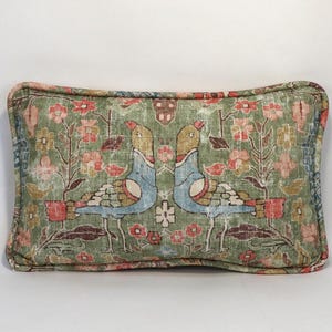 May include: Rectangular decorative pillow with a green background and a floral and bird pattern. The pillow features a detailed design with birds, flowers, and foliage in shades of blue, red, and pink. The edges are trimmed with a contrasting border.