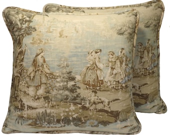 May include: Two decorative throw pillows with a beige linen fabric featuring a vintage-style print of women and a dog in a landscape setting. The print is in shades of brown, blue, and green.