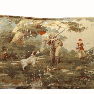 May include: A rectangular throw pillow with a beige background and a vintage hunting scene featuring two figures in a forest setting. The scene includes trees, a river, and a dog.