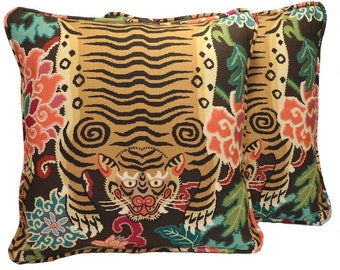 Könnte beinhalten: Zwei dekorative Kissen mit Tiger-Druck. Die Kissen zeigen einen braunen und goldenen Tiger mit schwarzen Streifen, umgeben von bunten Blumenmustern. Der Hintergrund ist dunkelbraun.