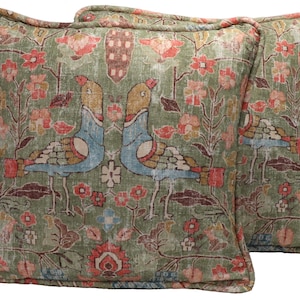 May include: Two square throw pillows with a faded, vintage look. The pillows feature a repeating pattern of birds, flowers, and foliage in shades of green, blue, red, and yellow. The pillows have a contrasting border.