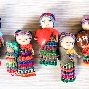 Puede incluir: Un conjunto de seis mu&ntilde;ecas artesanales coloridas con ropa y rostros bordados. Las mu&ntilde;ecas visten ropa tradicional guatemalteca y sostienen varios objetos, entre ellos un coraz&oacute;n, una taza y un libro.