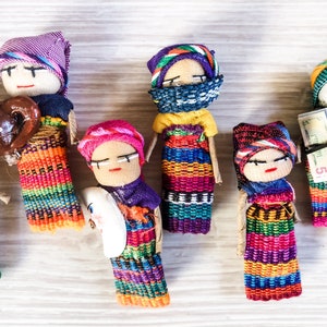 Puede incluir: Una colecci&oacute;n de mu&ntilde;ecas artesanales coloridas con intrincados patrones tejidos y accesorios &uacute;nicos. Las mu&ntilde;ecas visten ropa tradicional y sostienen objetos como una taza de caf&eacute; y un billete de dinero.