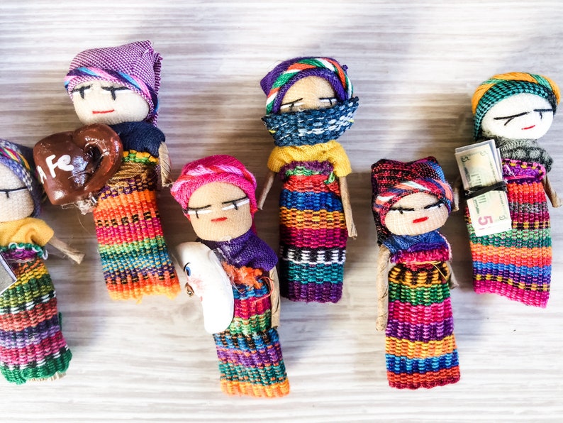 Puede incluir: Una colecci&oacute;n de mu&ntilde;ecas artesanales coloridas con intrincados patrones tejidos y accesorios &uacute;nicos. Las mu&ntilde;ecas visten ropa tradicional y sostienen objetos como una taza de caf&eacute; y un billete de dinero.