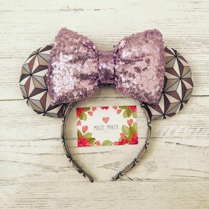May include: Purple sequin Minnie Mouse ears with a geometric pattern on the ears and a grey headband. The headband has a small tag that says "Magic Maker".