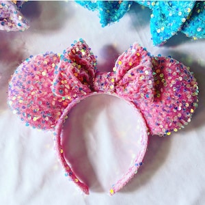 May include: Pink velvet mouse ears with iridescent sequins. The ears are attached to a headband.