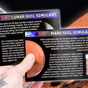 May include: Two small glass vials containing simulated lunar and Martian soil. The vials are labeled "Lunar Soil Simulant" and "Mars Soil Simulant". The text describes the use of these simulants in NASA research.