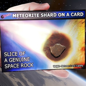 Könnte beinhalten: Eine Karte mit einem Meteoritensplitter darauf. Die Karte zeigt ein Bild eines Meteors, der in die Atmosphäre eindringt, und den Text "METEORITE SHARD ON A CARD", "SLICE OF A GENUINE SPACE ROCK" und "Weight - Between 3 and 5 grams".