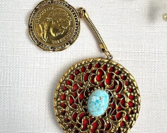 May include: A vintage gold-toned pendant with a coin-like element and a circular filigree design. The pendant features a red backing and a turquoise-colored stone. The coin-like element has a profile of a person.