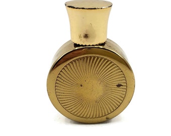 May include: A gold round perfume bottle with a gold cap and a sunburst design on the front.
