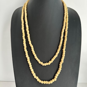 May include: Two strands of a cream-coloured beaded necklace. The beads are small and round, with a carved floral design. The necklace is displayed on a black mannequin.