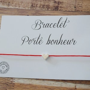 Peut inclure: Bracelet en cordon rouge avec un charm en forme de cœur argenté. La carte indique "Bracelet Porte bonheur" et "Handmade with Love".