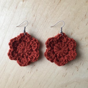 May include: A pair of crocheted flower earrings in a burnt orange colour with silver hooks.