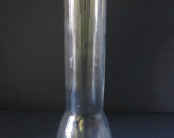 May include: A clear glass oil lamp chimney with a round base and a tall, cylindrical body.