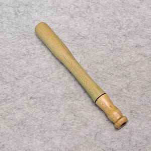 May include: A light-colored wooden tool with a long, cylindrical handle that tapers toward a rounded, bulbous end. The wood grain is visible throughout the surface, and a thin, dark ring separates the handle from the shaped tip of the object.
