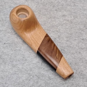 May include: A wooden pipe with a light brown finish and a dark brown inlay. The pipe has a rounded bowl and a straight stem. The pipe is made of two different types of wood.