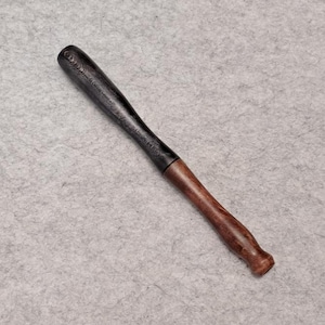 May include: A slender, elongated wooden tool featuring a two-toned design. The upper portion is finished in a dark, matte black, while the lower handle section displays a natural, polished reddish-brown wood grain with a rounded, tapered end.
