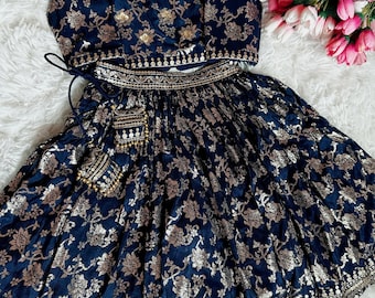 May include: A navy blue and gold embroidered skirt and top set. The skirt has a floral pattern and the top has a round neckline. The set is decorated with gold sequins and beads.