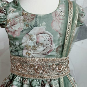May include: A green and pink floral print dress with a gold embroidered belt and a matching sheer dupatta. The dress has a round neckline and short sleeves.