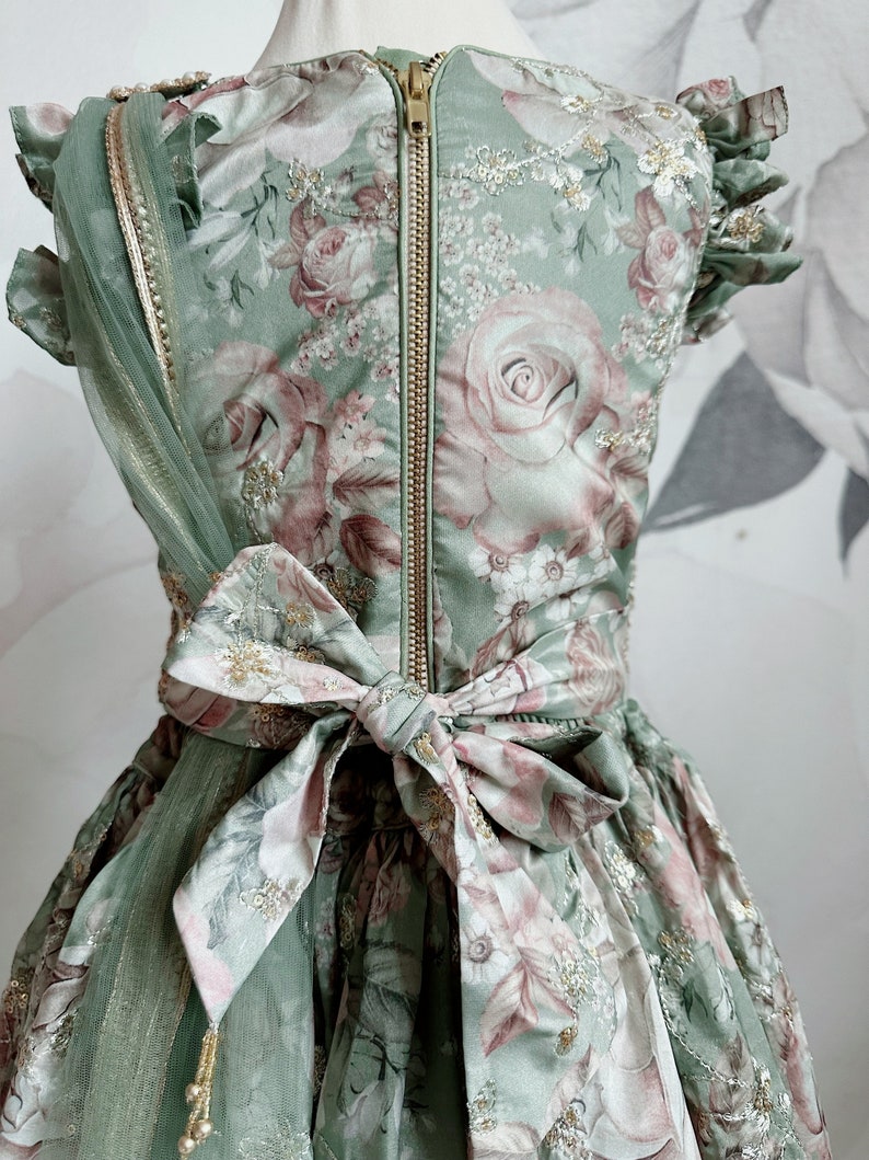 May include: A green floral dress with a gold zipper and a matching sash tied in a bow at the waist. The dress has a tulle overlay and gold embellishments.