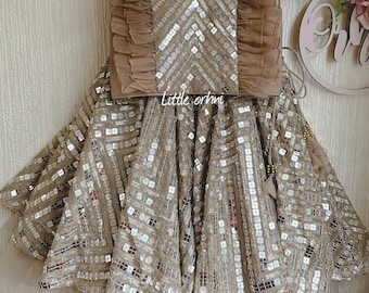 May include: A brown and silver sequined skirt and top set for a young girl. The skirt has a ruffled hem and the top has a ruffled neckline. The set is decorated with a geometric pattern.