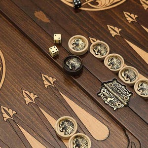 Puede incluir: Un tablero de backgammon de madera con intrincados tallados y una incrustación de latón. El tablero está abierto y muestra la superficie de juego con fichas blancas y negras. El tablero está hecho de madera oscura con una incrustación de madera clara.