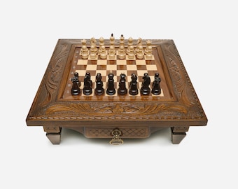 May include: A wooden chessboard with intricate carvings on the frame. The board has a traditional checkered pattern and is set up for a game of chess with black and white pieces.